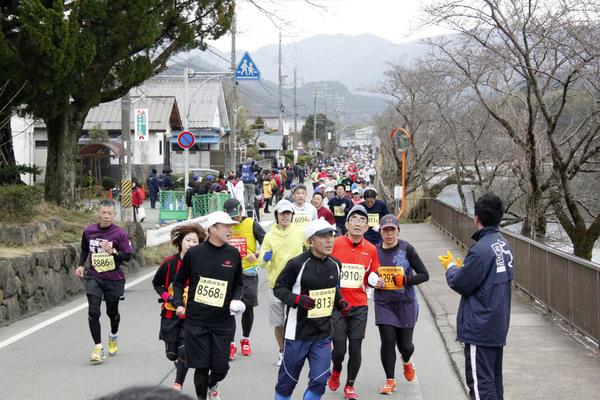 右側の沿道にジャンバーをきた男性が手を叩きながら応援していて、その横を大勢のランナー達が走っている写真